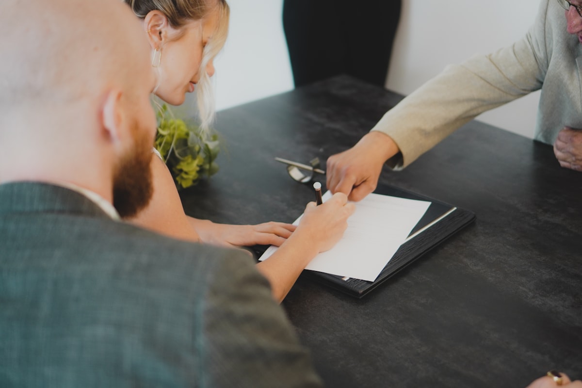 A couple signing paperwork at a table while an agent points to where to sign